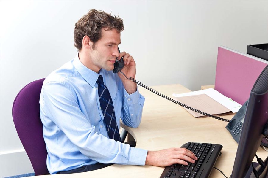 man talking on phone while typing on computer